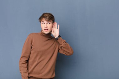 Genç sarışın adam gülümsüyor, tuhaf bir şekilde yan tarafa bakıyor, dedikoduları dinlemeye çalışıyor ya da duvarda izole edilmiş bir sırrı duymaya çalışıyor.