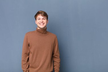 Genç sarışın adam mutlu ve şapşal görünüyor. Geniş, eğlenceli, kaçık bir gülüşü ve düz duvara karşı tamamen izole edilmiş gözleri var.