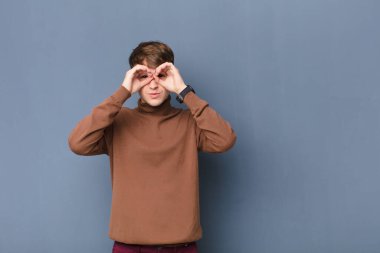 Genç sarışın adam şok olmuş, şaşırmış ve şaşırmış hissediyor. Elinde şaşırmış, inançsız bir şekilde duvara yaslanmış gözlük tutuyor.