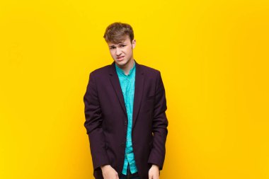 young blonde man feeling puzzled and confused, with a dumb, stunned expression looking at something unexpected isolated against flat wall