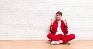 Genç sarışın adam endişeyle şans diliyor ve endişeli bir bakışla yerde oturuyor.