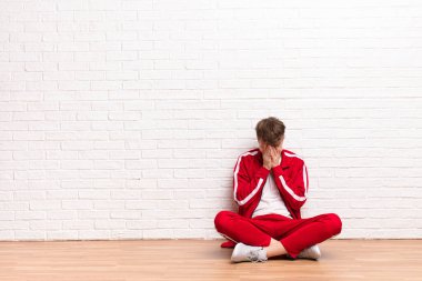 Genç sarışın adam üzgün, hayal kırıklığına uğramış bir bakışla gözlerini kapatıyor, ağlıyor, yere bakıyor.