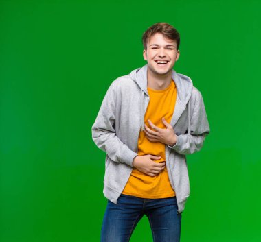 Genç sarışın adam komik bir şakaya yüksek sesle gülüyor, mutlu ve neşeli hissediyor, kroma tuşlu duvara karşı eğleniyor.