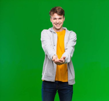 Genç sarışın adam mutlu bir şekilde gülümsüyor. Cana yakın, kendinden emin, pozitif bakışlı. Renkli duvara karşı bir nesne ya da konsept sunuyor ve gösteriyor.