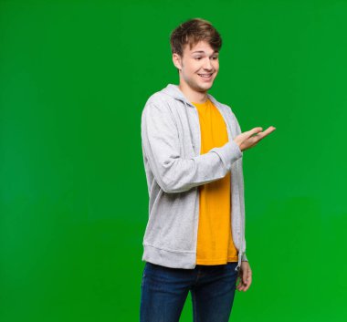 Genç sarışın adam neşeyle gülümsüyor, mutlu hissediyor ve fotokopi uzayda elini kroma tuşuna yaslamış bir konsept gösteriyor.