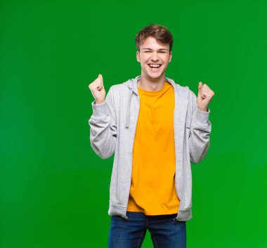 Genç sarışın adam son derece mutlu ve şaşırmış görünüyor, başarıyı kutluyor, bağırıyor ve kroma tuşuna karşı zıplıyor.