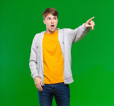 Genç sarışın adam şok olmuş ve şaşırmış hissediyor, şaşkınlıkla yukarı bakıyor, şaşırmış, ağzı açık bir şekilde Chroma anahtar duvarına bakıyor