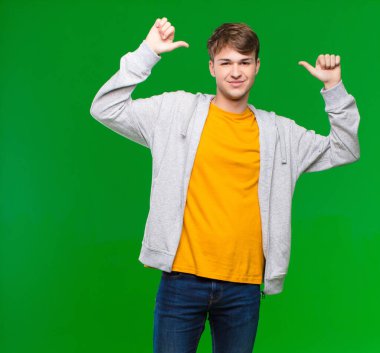 Genç sarışın adam gururlu, kibirli ve kendinden emin, tatmin olmuş ve başarılı görünüyor, kendini kroma tuşlu duvara işaret ediyor.