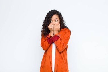 Genç siyah kadın endişeli, gergin, stresli ve korkmuş görünüyor, tırnaklarını yiyor ve beyaz duvara karşı yanal fotokopi alanı arıyor.