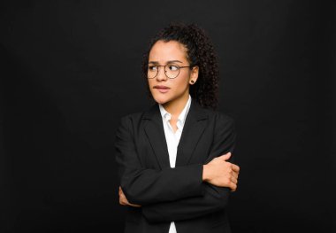 Genç siyahi kadın şüpheye düşüyor ya da düşünüyor, dudağını ısırıyor ve kendini güvensiz ve gergin hissediyor, siyah duvara karşı uzayı kopyalamak istiyor.