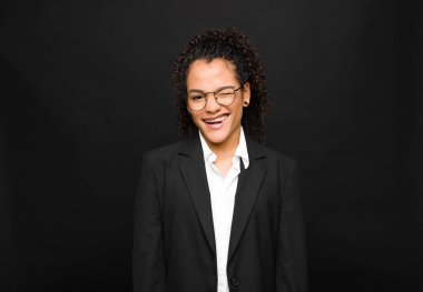 Genç siyah kadın mutlu ve arkadaş canlısı görünüyor, gülümsüyor ve siyah duvara karşı pozitif bir tavırla sana göz kırpıyor.