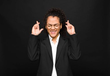 Genç siyahi kadın gülümsüyor ve endişeyle iki parmağını çapraz yapıyor. Endişeli ve kara duvara karşı iyi şanslar diliyor veya umut ediyor.