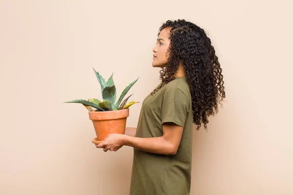 young black woman on profile view looking to copy space ahead, thinking, imagining or daydreaming holding a cactus