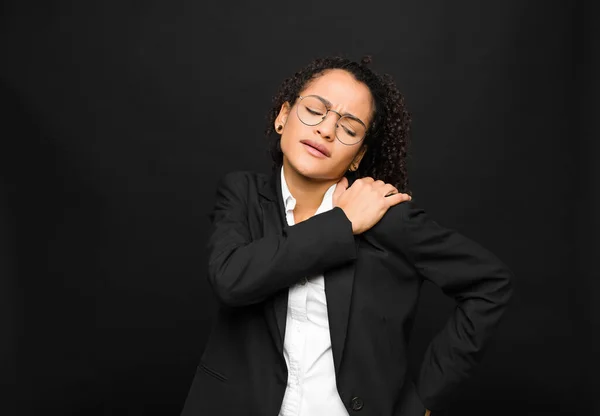 若い黒人女性は疲れ ストレス 憂うつで 黒い壁に背中や首の痛みに苦しんでいます — ストック写真