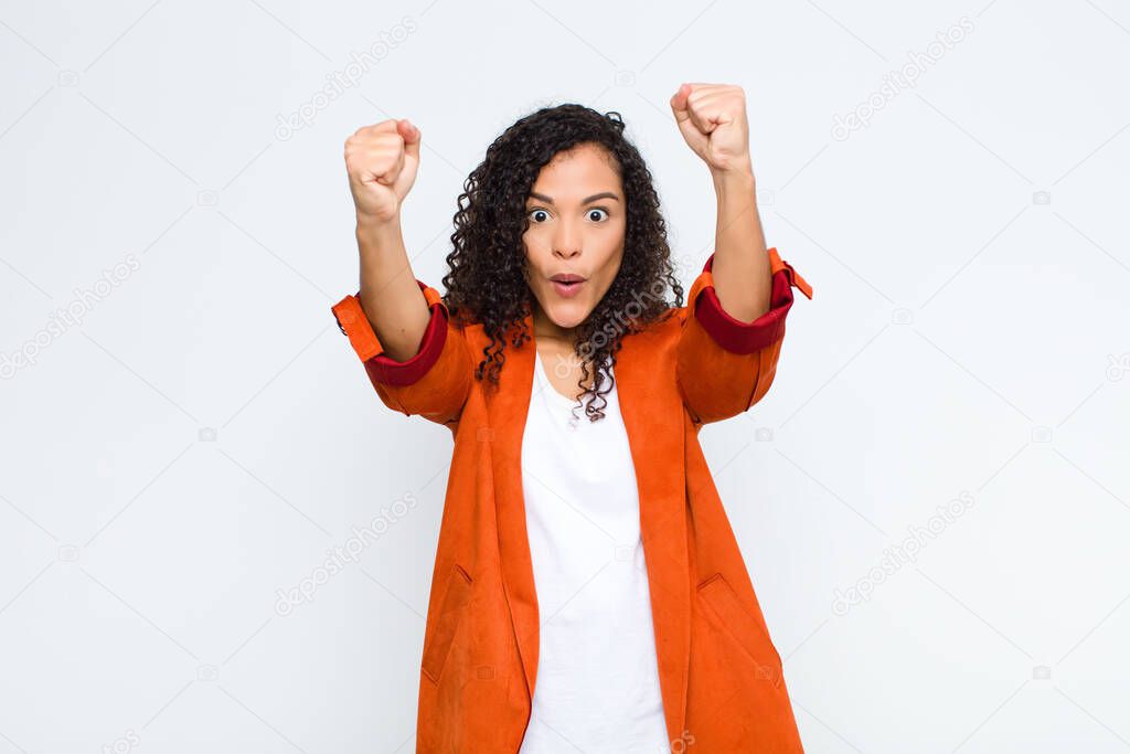 young black woman celebrating an unbelievable success like a winner, looking excited and happy saying take that! against white wall