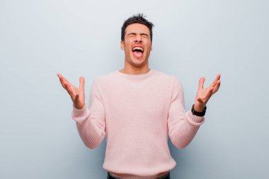 Genç Arap adam öfkeyle bağırıyor, stres altında ve elleri havada neden gri duvara yaslandığımı söylüyor.