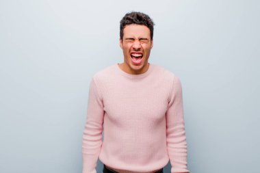 Genç Arap adam saldırganca bağırıyor, çok kızgın, hayal kırıklığına uğramış, öfkeli ya da kızgın görünüyor, gri duvara karşı hayır diye bağırıyor.