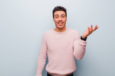 Genç Arap adam kendini mutlu, şaşırmış ve neşeli hissediyor, olumlu bir tavırla gülümsüyor, gri duvara karşı bir çözüm ya da fikir buluyor.