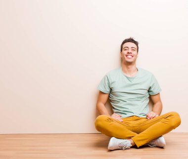 Genç Arap adam mutlu ve şapşal görünüyor. Geniş, eğlenceli, kaçık bir gülüşü ve gözleri açık yerde oturuyor.