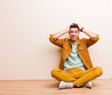 Genç Arap adam hayal kırıklığına uğramış ve sıkılmış hissediyor, başarısızlıktan bıkmış ve bıkmış, sıkıcı işlerden bıkmış, yerde oturuyor.