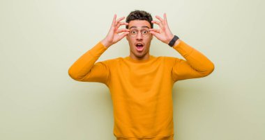 Genç Arap adam şok olmuş, şaşırmış ve şaşırmış hissediyor. Elinde hayret dolu, inanmayan bir bakışla düz duvara bakıyor.