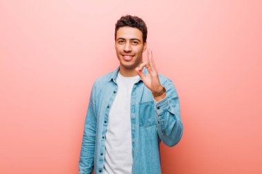 Genç Arap adam kendini mutlu, rahat ve tatmin olmuş hissediyor. Güzel bir jestle onaylıyor. Pembe duvara gülümsüyor.