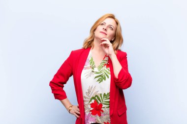 Orta yaşlı bir kadın mutlu bir şekilde gülümsüyor ve hayal kuruyor ya da şüphe ediyor.