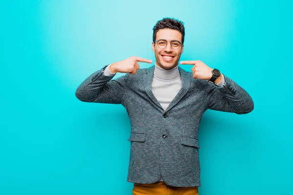 自信を持って笑顔を見せる若いアラビア人男性肯定的でリラックスした青い壁に対する満足した態度 — ストック写真