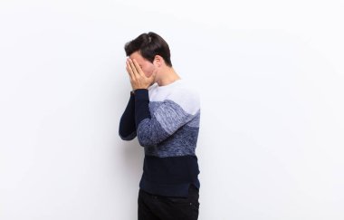 Genç yakışıklı adam, üzgün, hayal kırıklığına uğramış bakışlarıyla gözlerini kapıyor. Ağlıyor, beyaz duvara yan bakıyor.