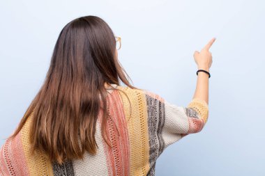 Genç ve güzel bir kadın dikilip objeyi işaret ediyor. Kopyalama alanı, dikiz açısı mavi duvara karşı.