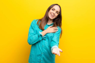 Genç ve güzel bir kadın mutlu ve aşık, bir eli kalbinin yanında, diğeri ise turuncu duvarın önünde uzanıyor.