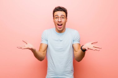 Genç Arap adam son derece şok olmuş, şaşırmış, endişeli ve paniklemiş hissediyor. Pembe duvara karşı stresli ve dehşetli bir bakışla bakıyor.