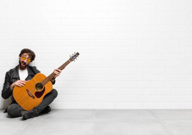 young musician man feeling puzzled and confused, with a dumb, stunned expression looking at something unexpected with a guitar, rock and roll concept