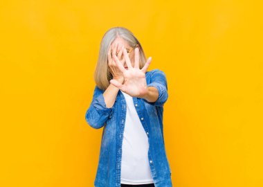 senior or middle age pretty woman covering face with hand and putting other hand up front to stop camera, refusing photos or pictures clipart