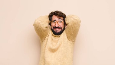 Havalı genç adam stresli, endişeli, endişeli ya da korkmuş, elleri başının üstünde, düz duvara karşı panikliyor.