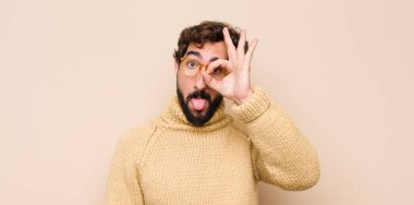 Genç havalı adam mutlu bir şekilde gülümsüyor, şaka yapıyor ve gözetleme deliğinden bakıyor, düz duvara karşı sırları gözetliyor.