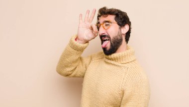 Genç havalı adam mutlu bir şekilde gülümsüyor, şaka yapıyor ve gözetleme deliğinden bakıyor, düz duvara karşı sırları gözetliyor.