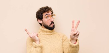 Genç, havalı bir adam gülümsüyor ve arkadaş canlısı görünüyor. İki ya da iki numarayı gösteriyor. Elleri önde, düz duvara doğru sayıyor.