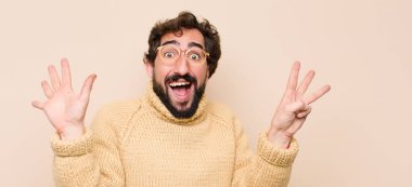 Havalı genç adam gülümsüyor ve arkadaş canlısı görünüyor. Sekiz ya da sekiz numarayı gösteriyor. Elleri önde, düz duvara doğru sayıyor.