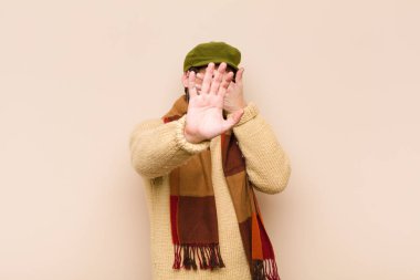 Genç, sakallı, sakallı, yüzü elle kaplayan ve diğer elini kamerayı durdurmak için öne koyan, fotoğraf ya da resimleri reddeden bir adam.