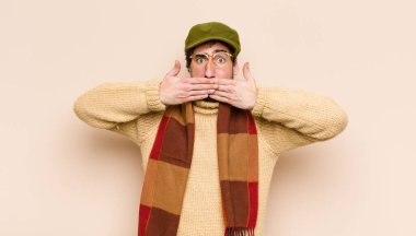 Genç havalı sakallı adam şok olmuş, şaşırmış bir ifadeyle ağzını kapatıyor, sır saklıyor ya da 