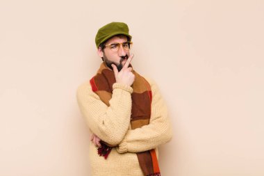 Genç havalı sakallı adam ciddi, düşünceli ve güvensiz görünüyor, bir kolu çapraz ve çenesi üzerinde, seçenekleri tartıyor.