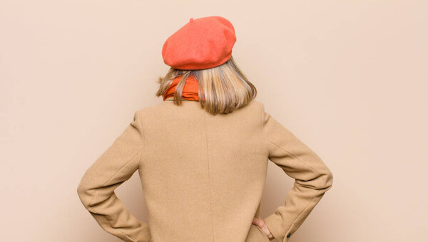 senior or middle age pretty woman feeling confused or full or doubts and questions, wondering, with hands on hips, rear view