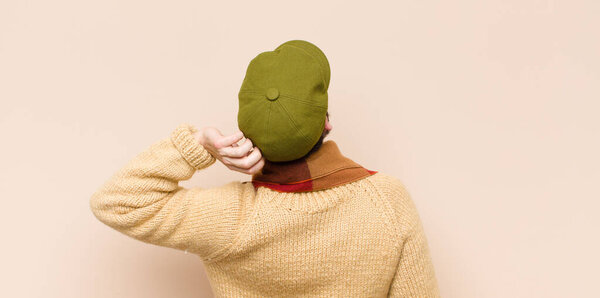 молодой прохладный бородатый человек чувствует себя невежественным и смущенным, думая решение, с рукой на бедре и другой на голове, вид сзади
