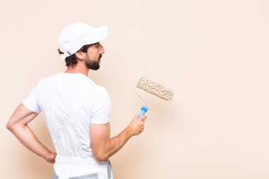 Genç ressam sakallı adam duvarları silindirle boyuyor.