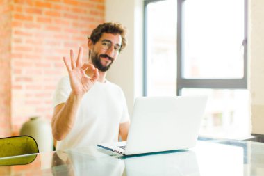 Dizüstü bilgisayarı olan genç sakallı adam kendini mutlu, rahat ve tatmin olmuş hissediyor.