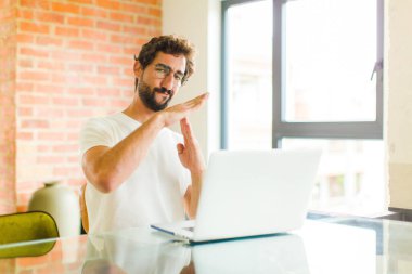 Dizüstü bilgisayarı olan genç sakallı adam ciddi, sert, kızgın ve canı sıkkın görünüyor.