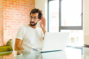 Dizüstü bilgisayarı olan genç sakallı bir adam tuhaf bir şekilde yan tarafa bakıyor. Dedikoduları dinlemeye ya da bir sırrı duymaya çalışıyor.