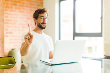 Dizüstü bilgisayarı olan genç sakallı bir adam gülümsüyor ve arkadaş canlısı görünüyor, bir numara ya da ilk eli önde, geriye doğru sayıyor.