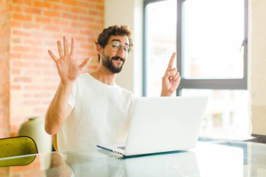 Bilgisayarlı genç sakallı adam gülümsüyor ve arkadaş canlısı görünüyor. Altı ya da altıncı numarayı gösteriyor. Eli önde, geri sayıyor.